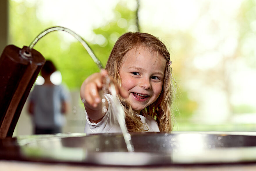 Ein Mädchen hält ihren Zeigefinger unter fließendes Wasser und lacht dabei