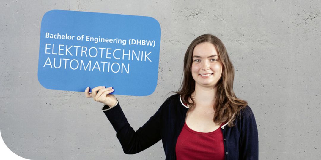 Junge Frau hält blaues Schild mit der Aufschrift „Bachelor of Engineering (DHBW) Elektrotechnik Automation“ hoch