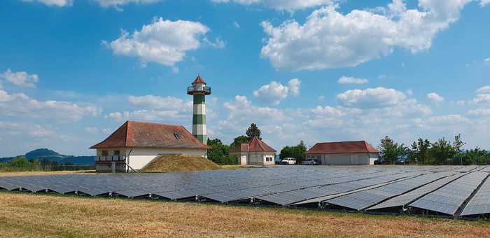 Feld mit vielen Solarmodulen, im Hintergrund ein Hof und Häuser